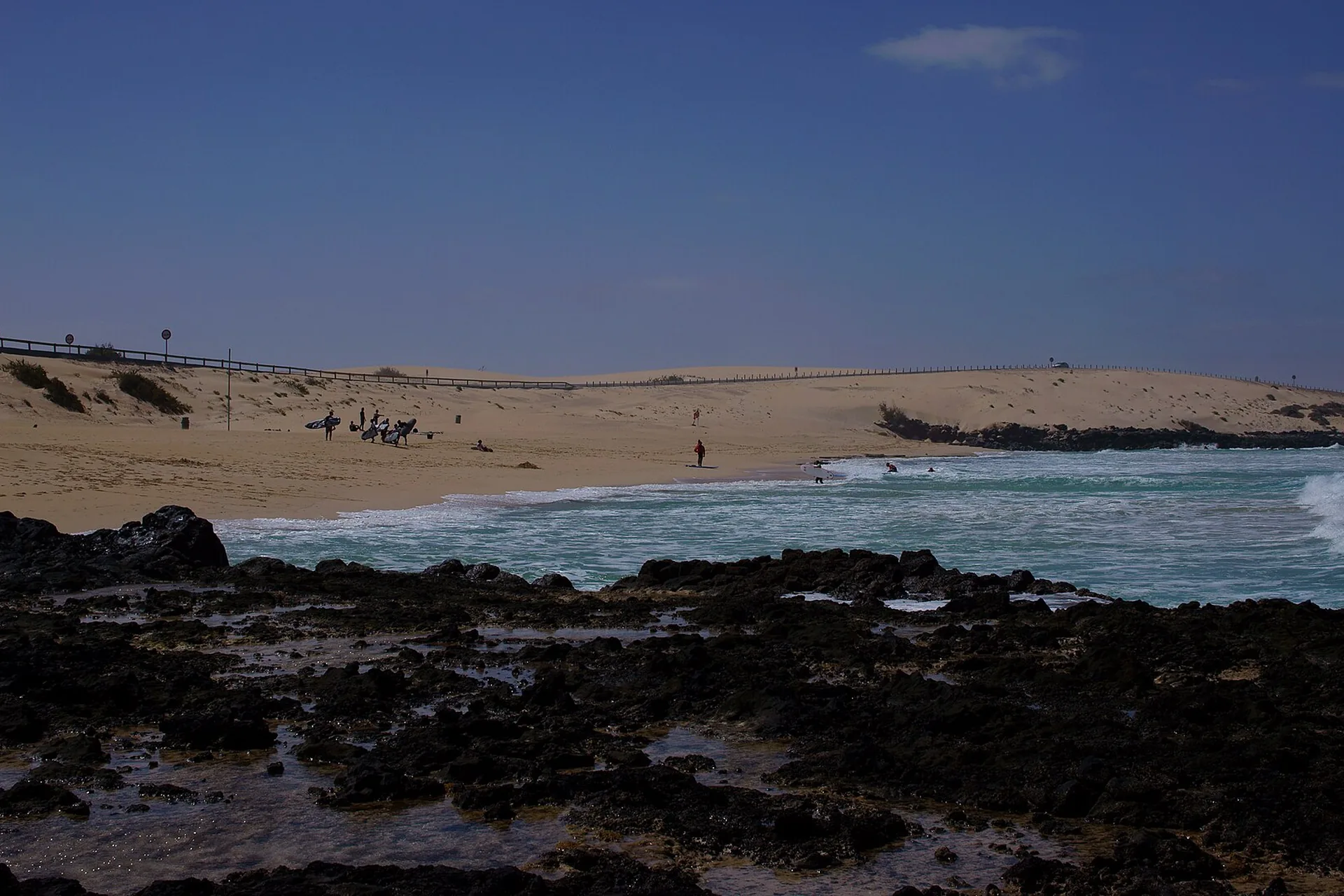 An expansive golden beach at Grandes Playas Corralejo, backed by rolling dunes, with a Riu hotel visible in the distance.