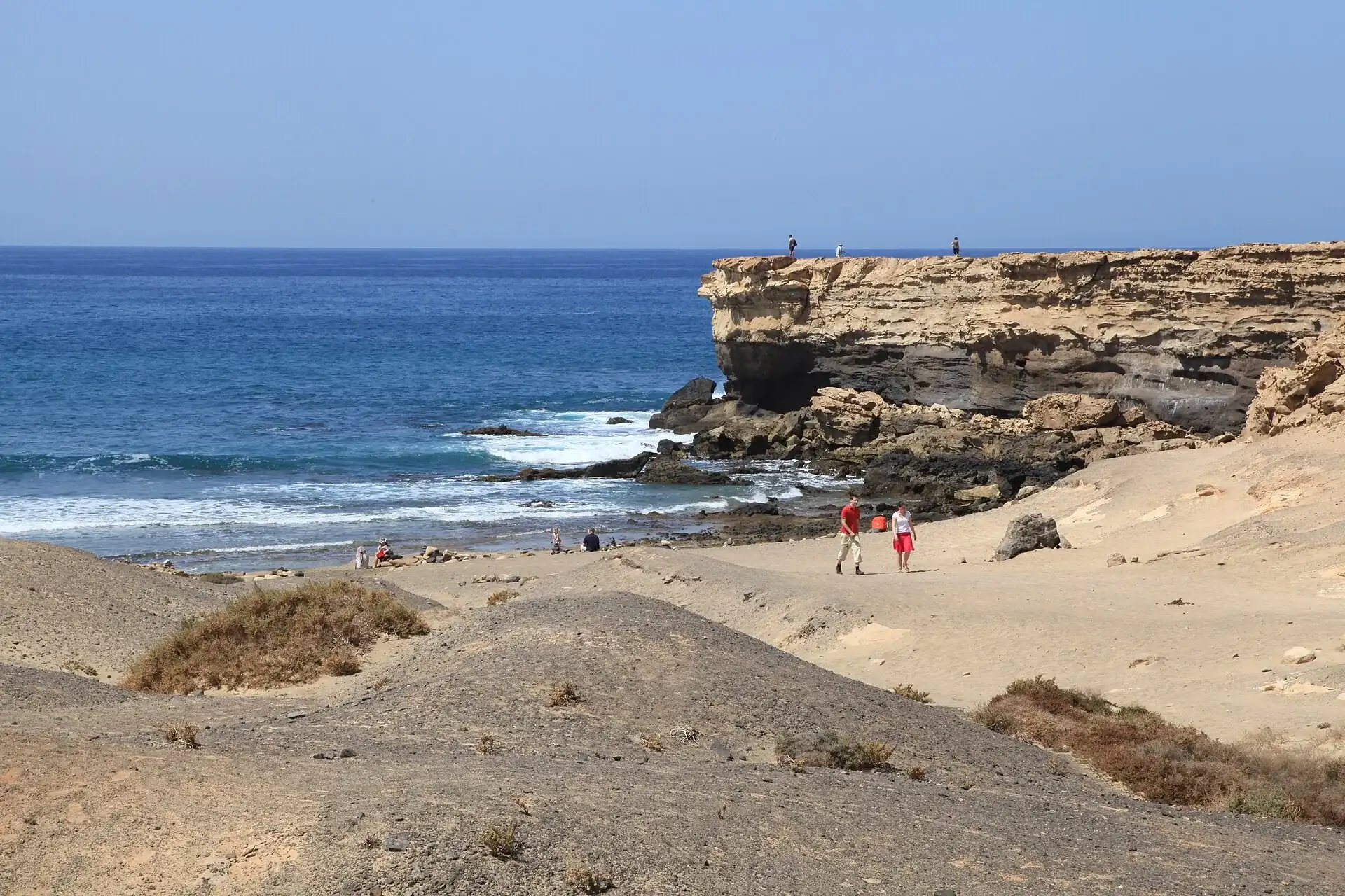 Ciemnozłota piaszczysta plaża Playa de la Pared na Fuerteventurze, z niskimi klifami i falami Atlantyku rozbijającymi si