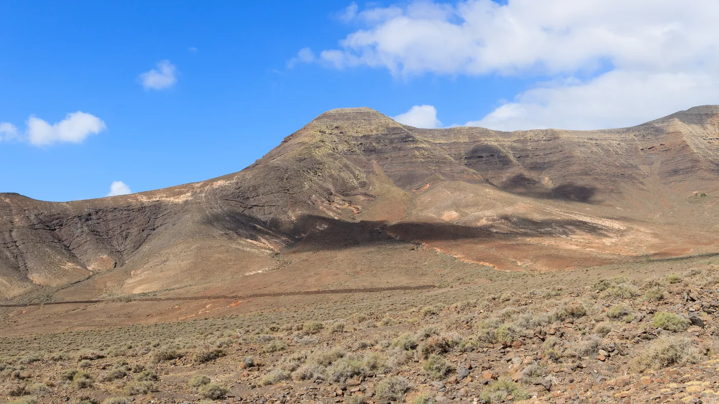 Un amplio valle volcánico y seco en el Gran Valle, con laderas veteadas en tonos marrones y rojizos bajo una cresta montañosa